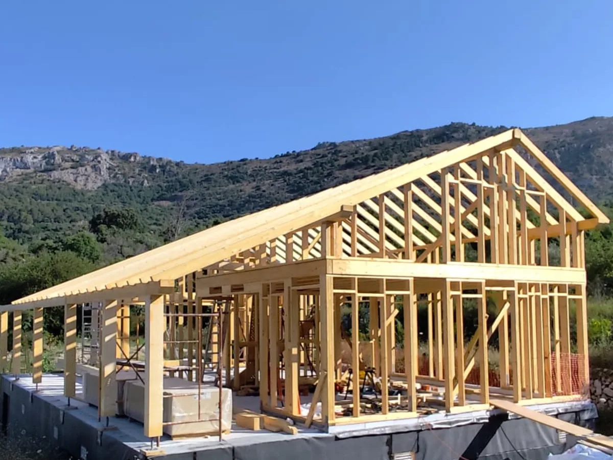 Estructura de madera de una vivienda montada sobre su cimentación, con la sierra al fondo